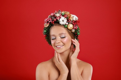 Photo of Beautiful young woman wearing Christmas wreath on red background