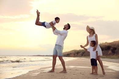 Photo of Happy family having fun on sandy beach near sea at sunset