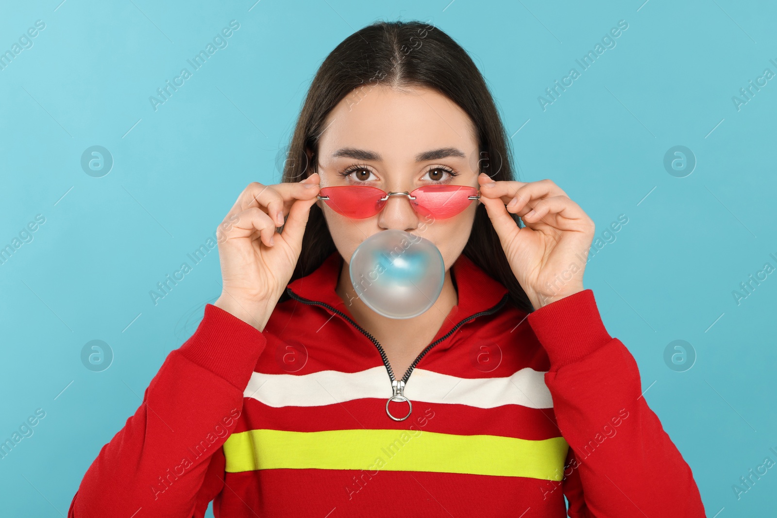 Photo of Beautiful young woman blowing bubble gum on light blue background