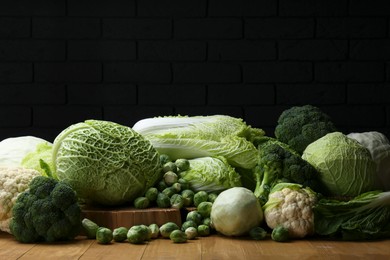 Many different types of fresh cabbage on wooden table near brick wall