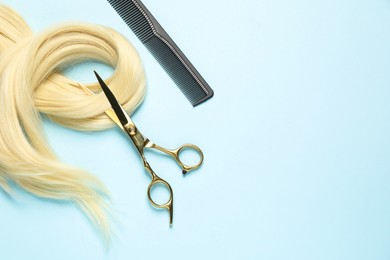 Professional hairdresser scissors and comb with blonde hair strand on light blue background, flat lay. Space for text