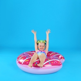 Photo of Cute little child in beachwear with inflatable ring on light blue background