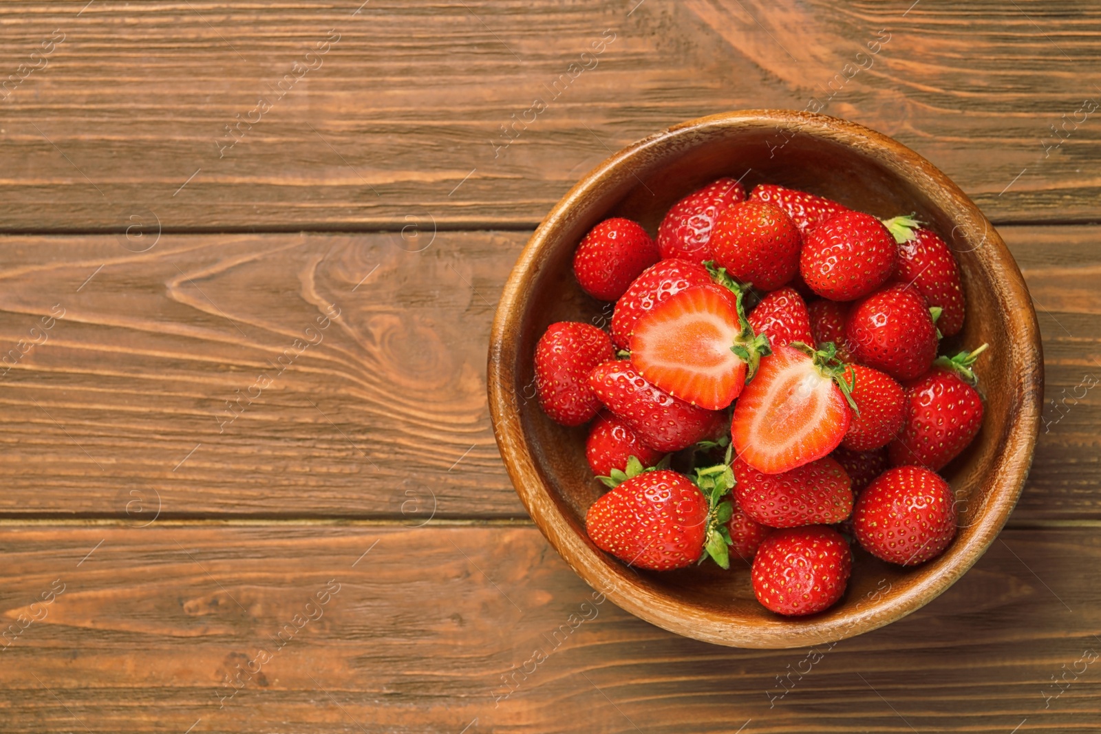 Photo of Bowl with ripe strawberries on wooden background, top view