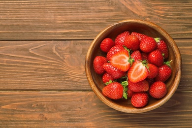 Photo of Bowl with ripe strawberries on wooden background, top view