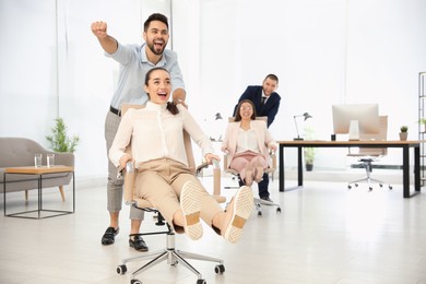 Happy office employees riding chairs at workplace