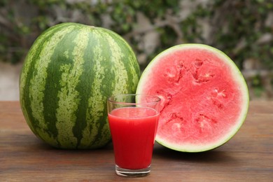 Photo of Delicious ripe watermelons and glass of fresh juice on wooden table outdoors