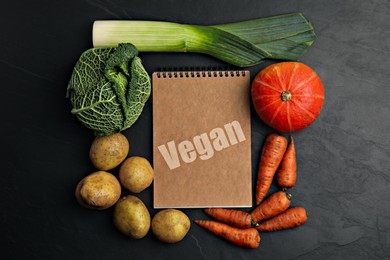 Image of Notebook with word Vegan and fresh vegetables on black background, flat lay