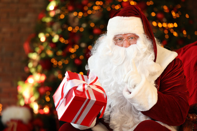 Photo of Santa Claus with gift near Christmas tree indoors