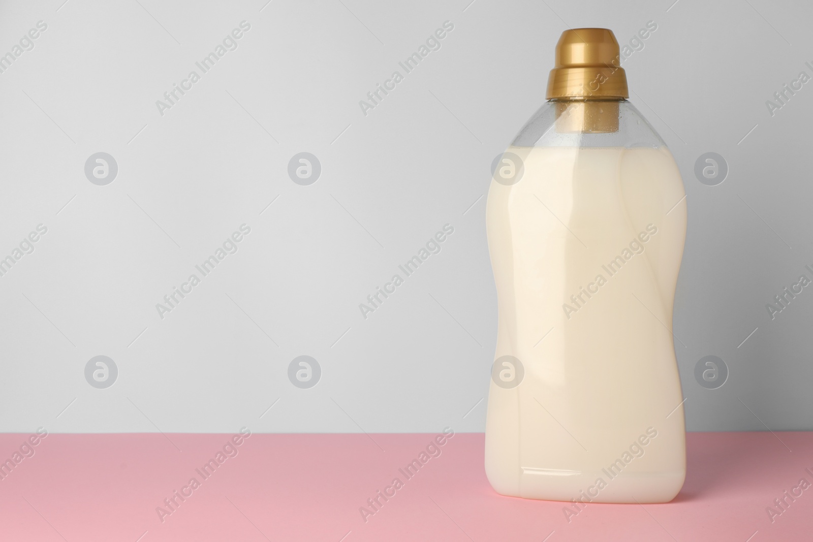 Photo of Bottle of fabric softener on pink table against light grey background, space for text