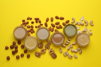 Photo of Different types of nut butter and ingredients on yellow background, flat lay