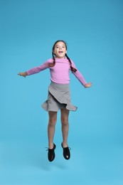 Photo of Cute schoolgirl jumping on light blue background