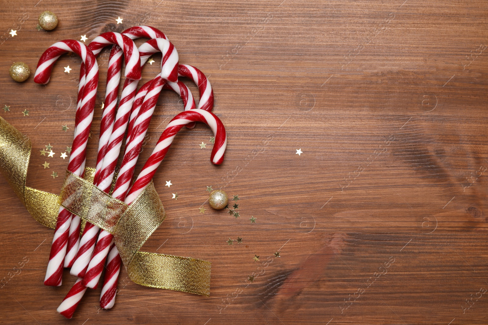 Photo of Sweet Christmas candy canes with golden ribbon and festive decor on wooden table, flat lay. Space for text