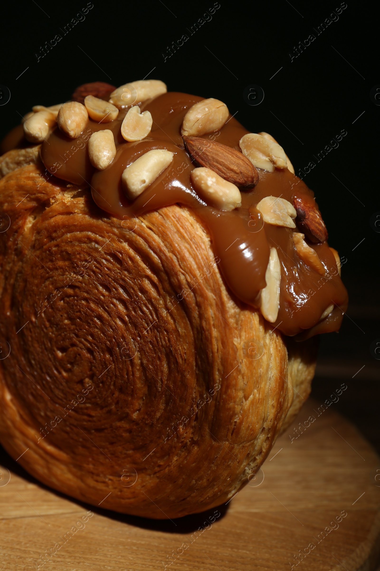 Photo of Round croissant with chocolate paste and nuts on wooden board, closeup. Tasty puff pastry