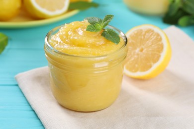 Delicious lemon curd in glass jar, fresh citrus fruit and mint on light blue wooden table, closeup