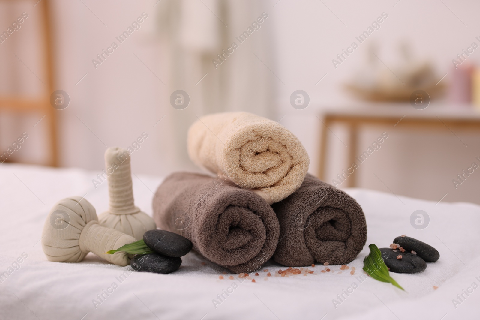 Photo of Spa stones, rolled towels and herbal bags on massage table indoors