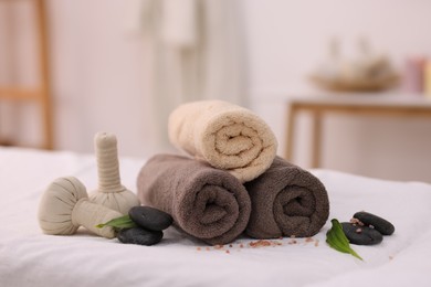 Spa stones, rolled towels and herbal bags on massage table indoors