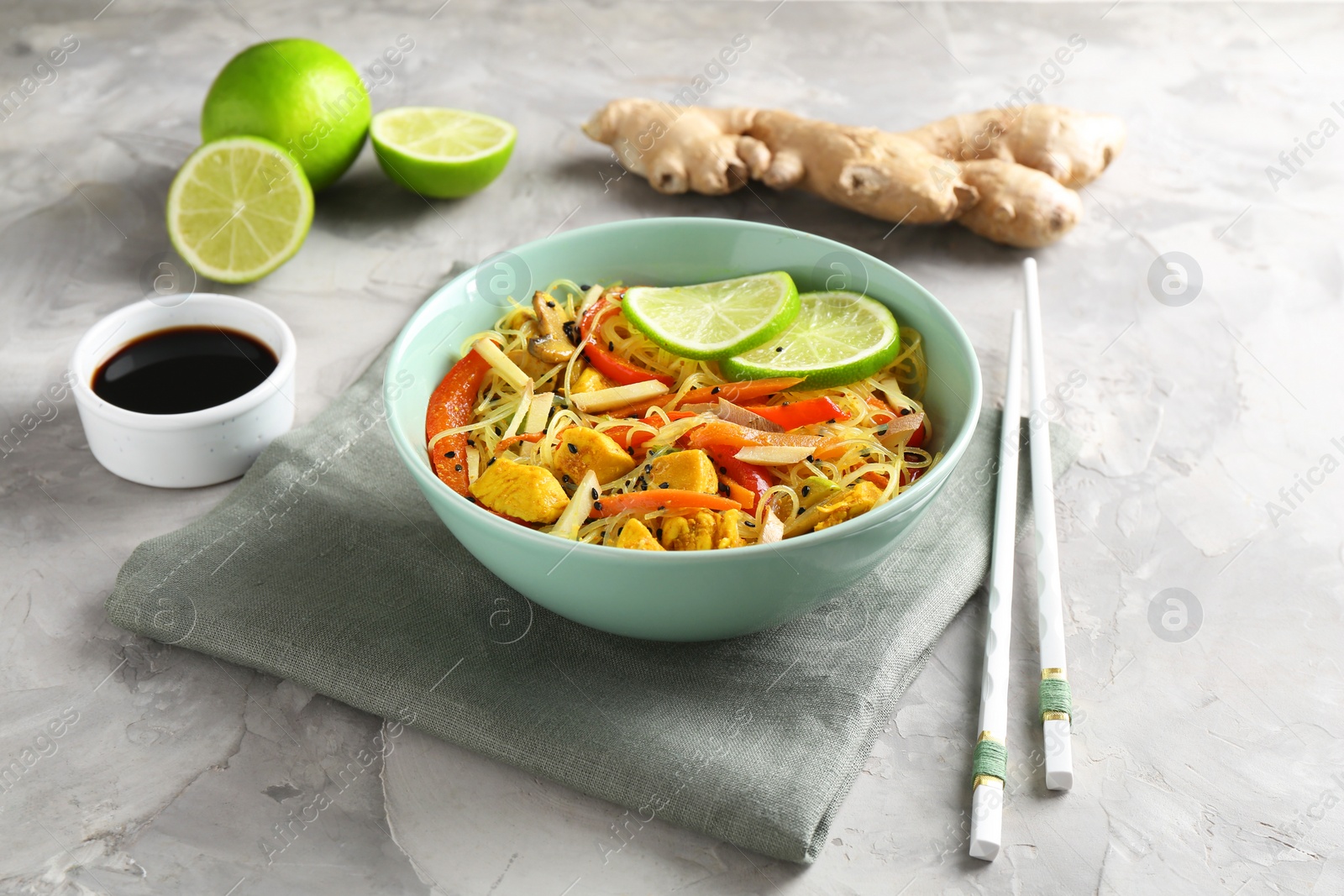 Photo of Stir-fry. Delicious cooked noodles with chicken and vegetables in bowl served on gray textured table