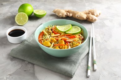 Photo of Stir-fry. Delicious cooked noodles with chicken and vegetables in bowl served on gray textured table