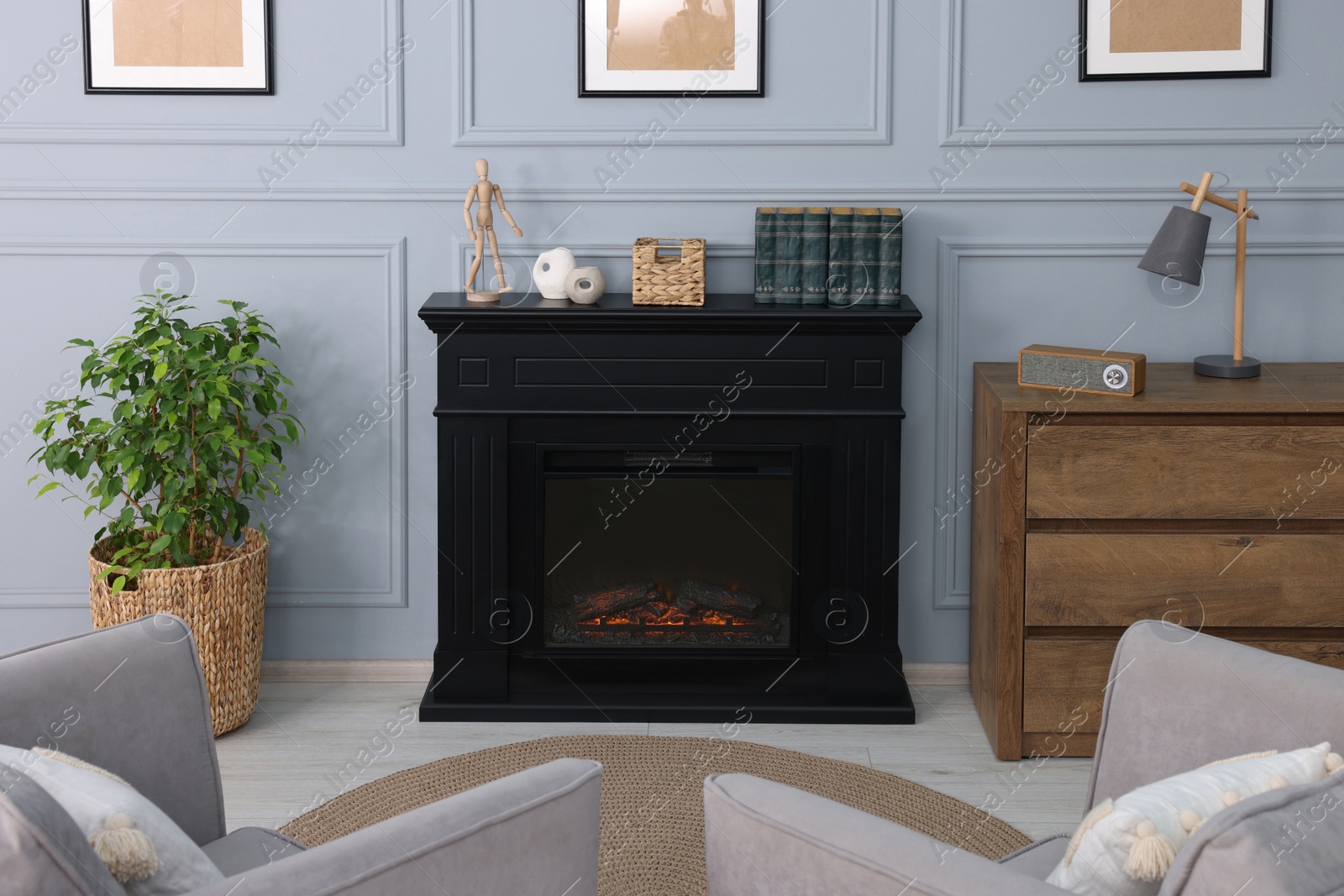 Photo of Black stylish fireplace between potted plant and chest of drawers in cosy living room