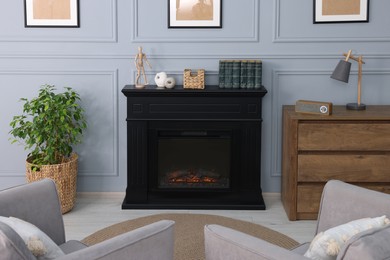 Black stylish fireplace between potted plant and chest of drawers in cosy living room