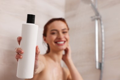 Happy young woman with bottle of shampoo in shower, selective focus. Space for text