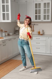 Woman with broom singing while cleaning in kitchen