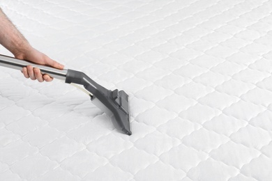 Man disinfecting mattress with vacuum cleaner, closeup. Space for text