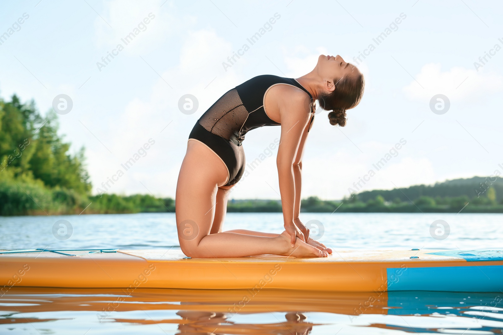 Photo of Young woman practicing yoga on color SUP board on river