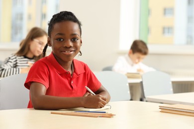 Photo of Portrait of smiling little boy studying in classroom at school. Space for text