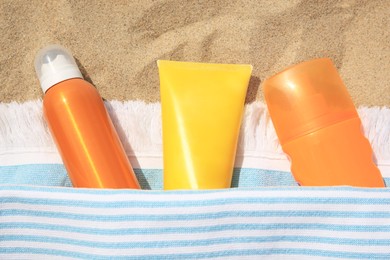 Photo of Sunscreens and towel on sand, flat lay. Sun protection care
