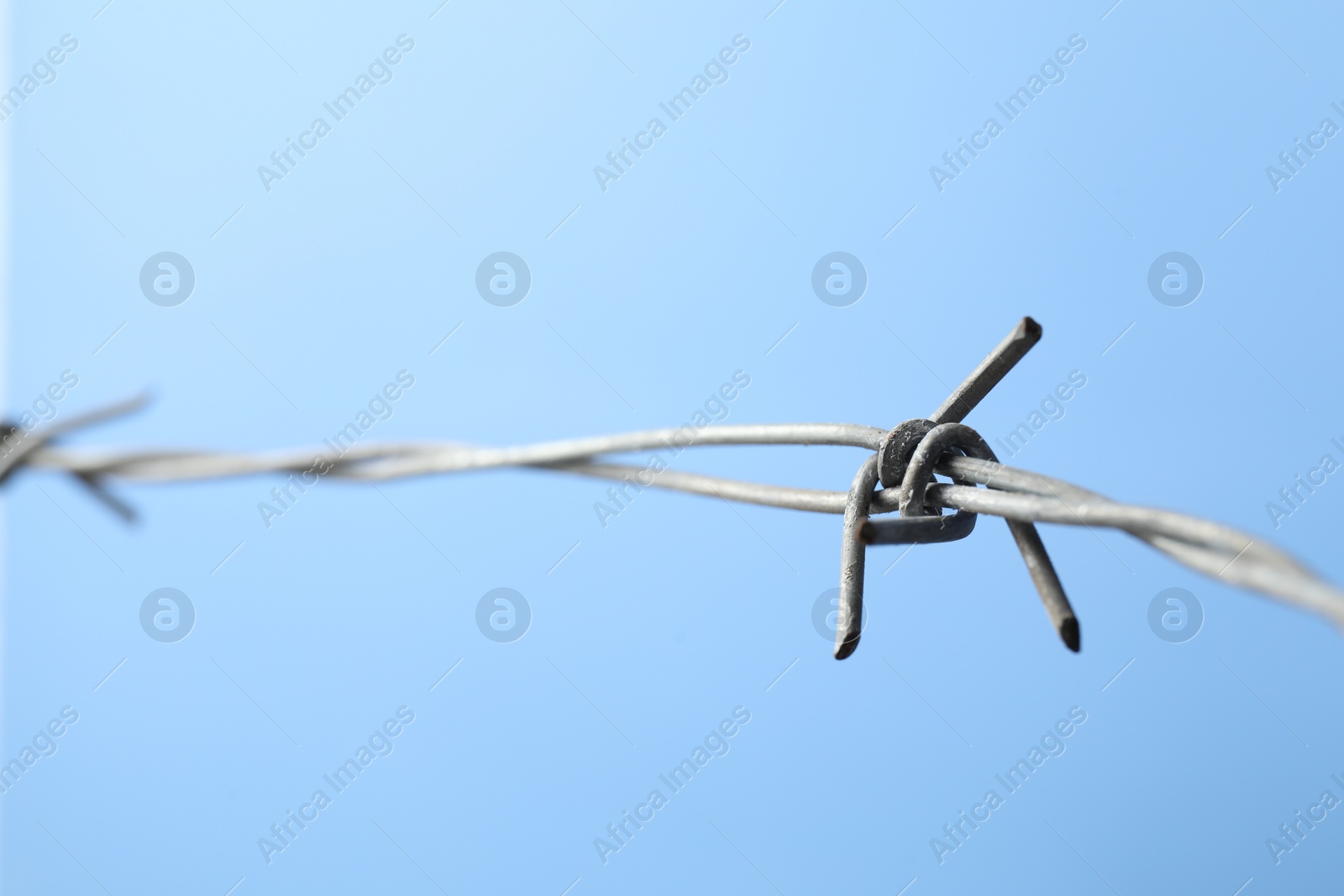 Photo of Metal barbed wire on light blue background, closeup