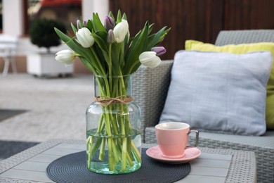 Photo of Beautiful bouquet of colorful tulips and cup with drink on rattan garden table outdoors