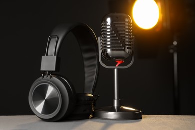 Photo of Vintage microphone and headphones on table against black background. Sound recording and reinforcement