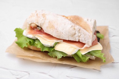 Tasty sandwich with brie cheese and prosciutto on white textured table, closeup