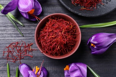 Dried saffron in bowl and crocus flowers on black wooden table, flat lay