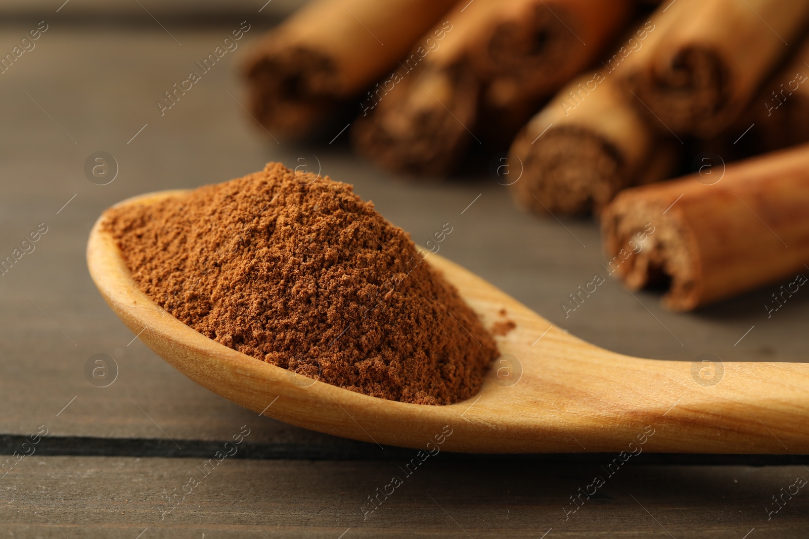 Photo of Spoon with cinnamon powder and sticks on wooden table, closeup