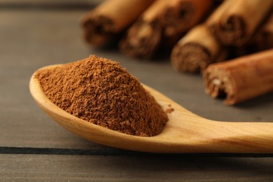 Spoon with cinnamon powder and sticks on wooden table, closeup