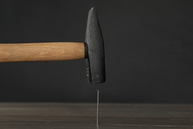 Hammering metal nail on wooden table against black background. Space for text