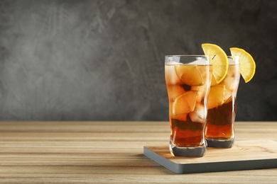 Glasses of tasty ice tea with lemon on wooden table against grey background, space for text