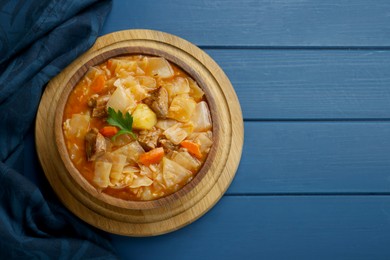 Photo of Tasty cabbage soup with meat, carrot and parsley on blue wooden table, top view. Space for text