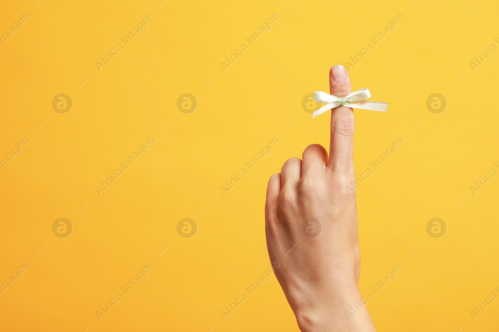 Photo of Woman showing index finger with tied bow as reminder on orange background, closeup. Space for text