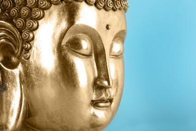 Photo of Beautiful golden Buddha sculpture on light blue background, closeup. Space for text