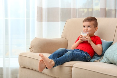 Photo of Cute little boy drinking milk on sofa at home