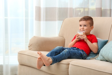 Cute little boy drinking milk on sofa at home