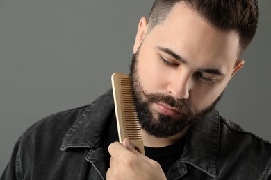 Photo of Handsome young man combing beard on grey background