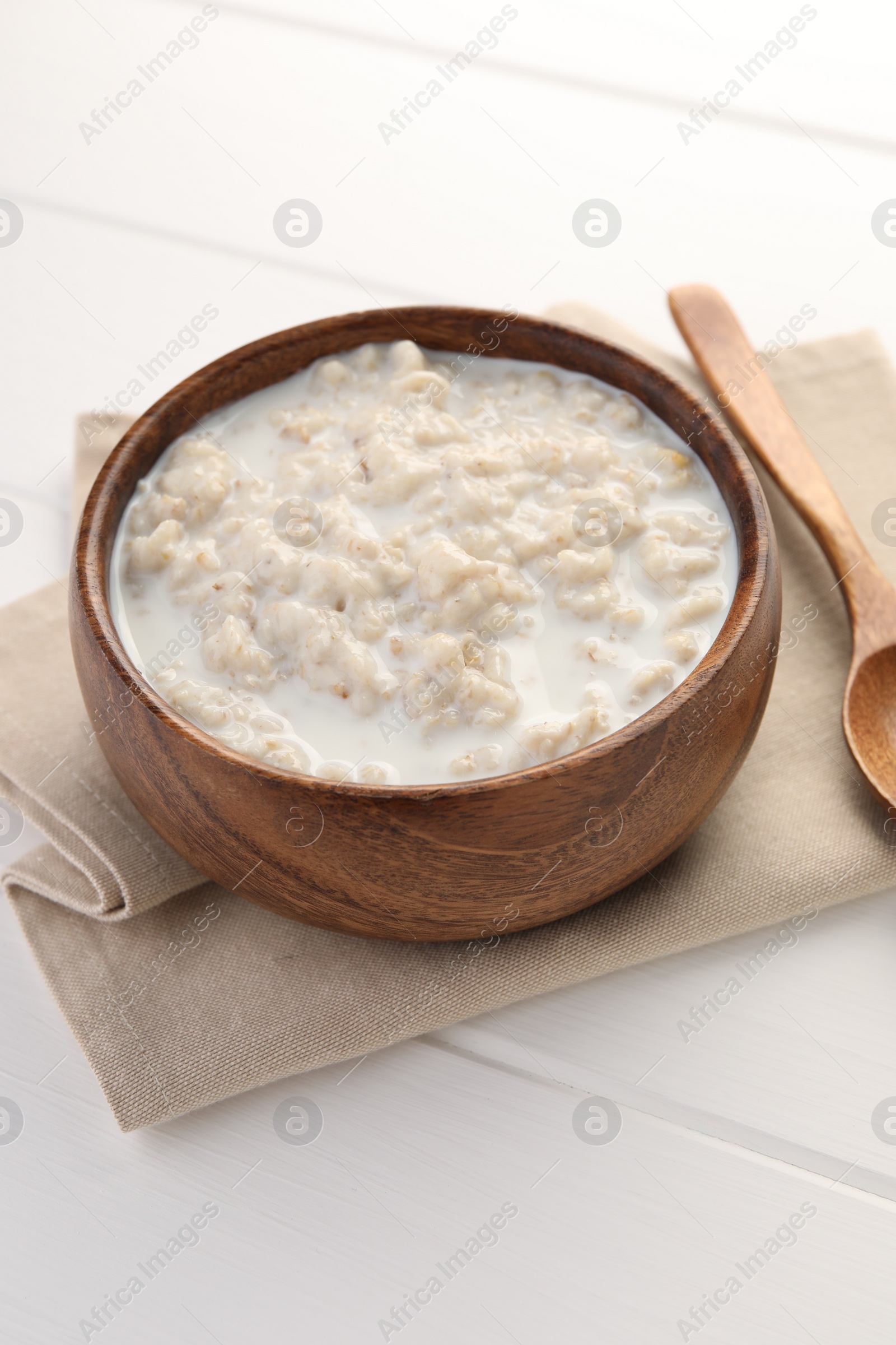 Photo of Tasty boiled oatmeal in bowl on white wooden table