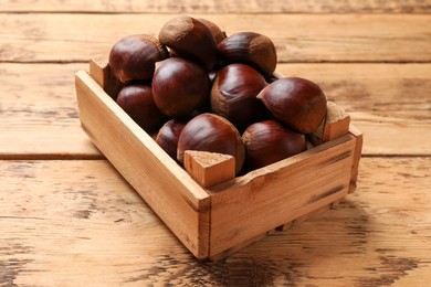 Photo of Sweet fresh edible chestnuts in crate on wooden table