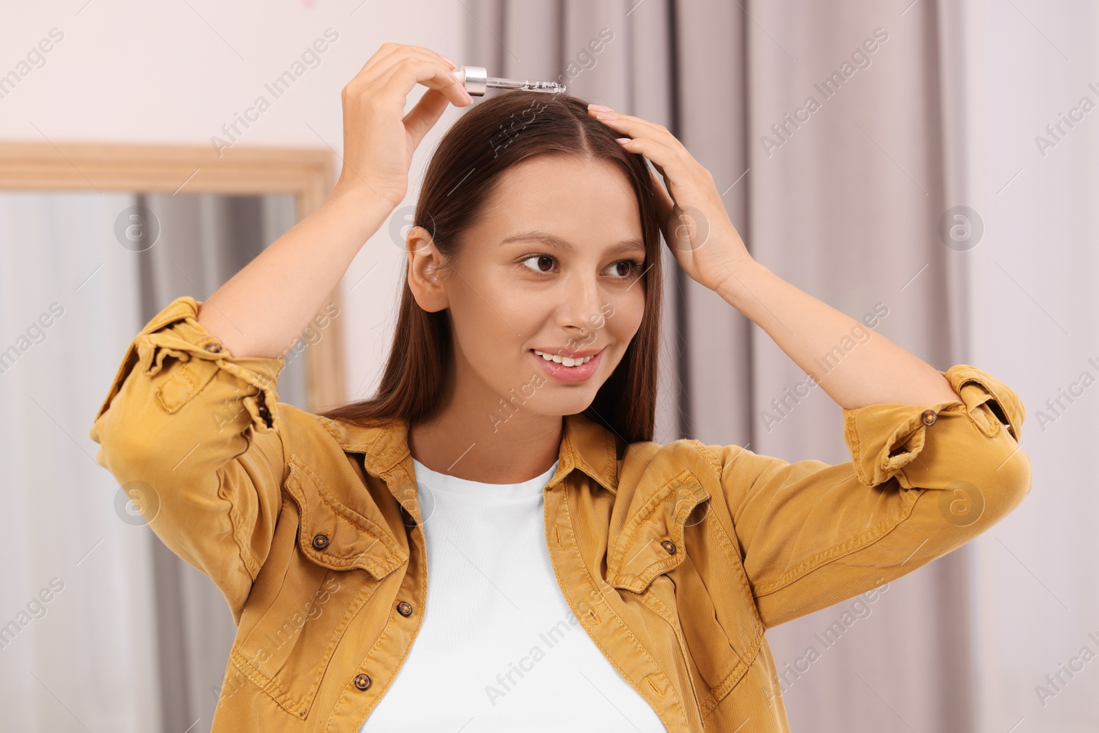 Photo of Beautiful woman applying serum onto hair indoors