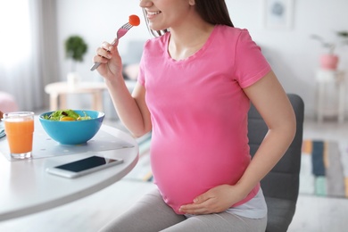 Photo of Young pregnant woman eating vegetable salad at table in kitchen