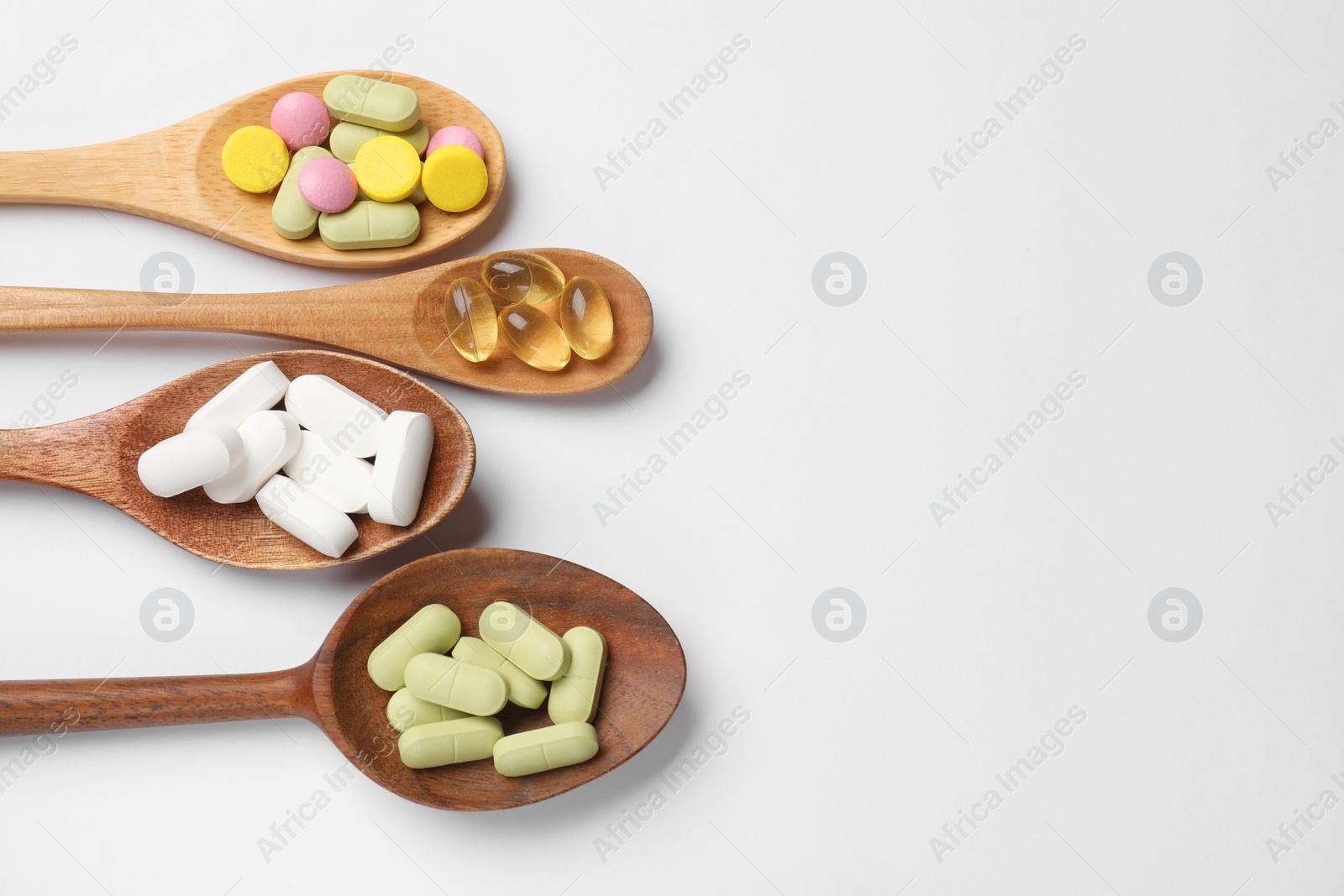 Photo of Different vitamin pills in wooden spoons on white background, flat lay. Space for text